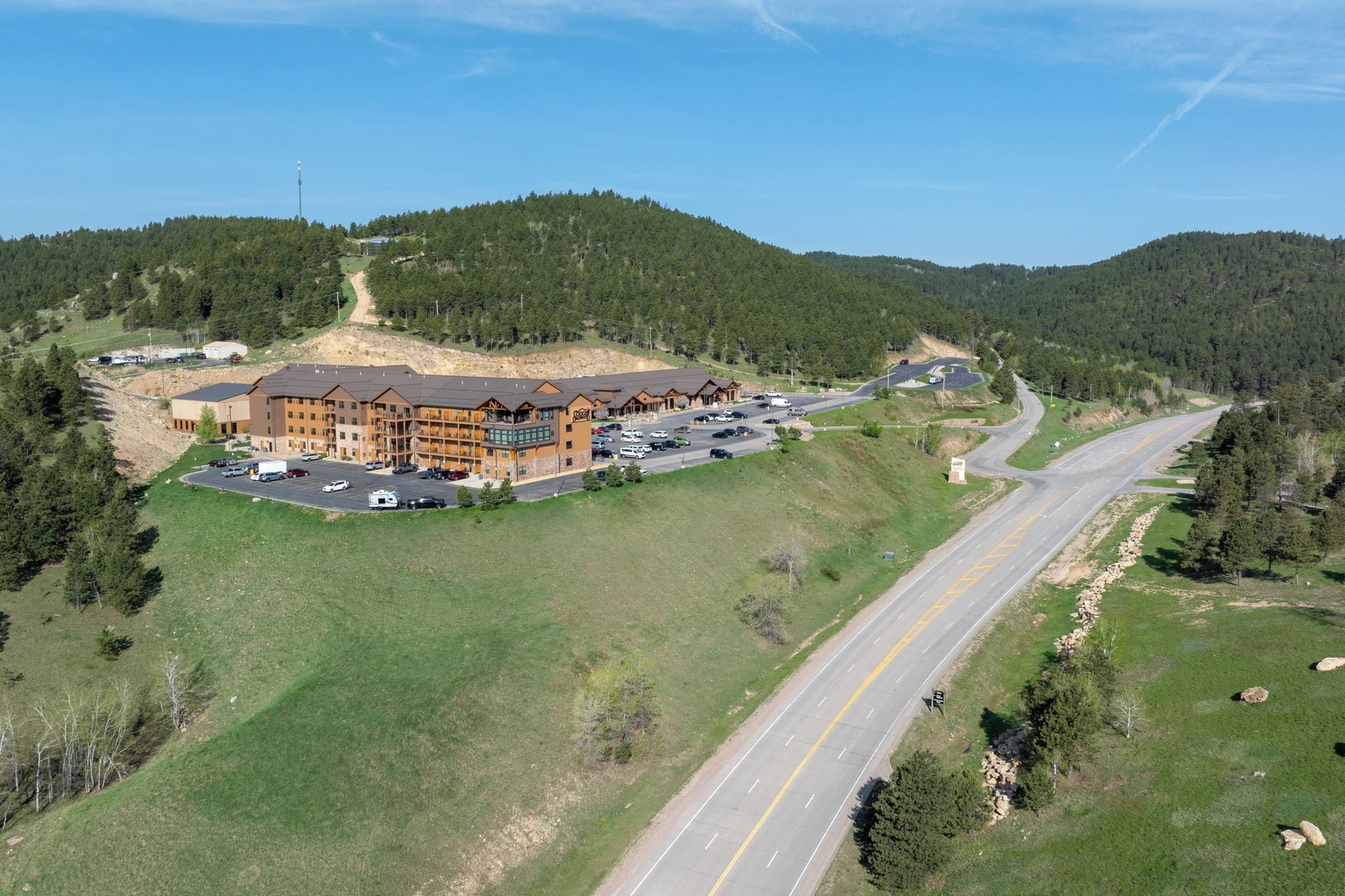 A lodge with multiple floors and a parking lot, surrounded by forested hills.