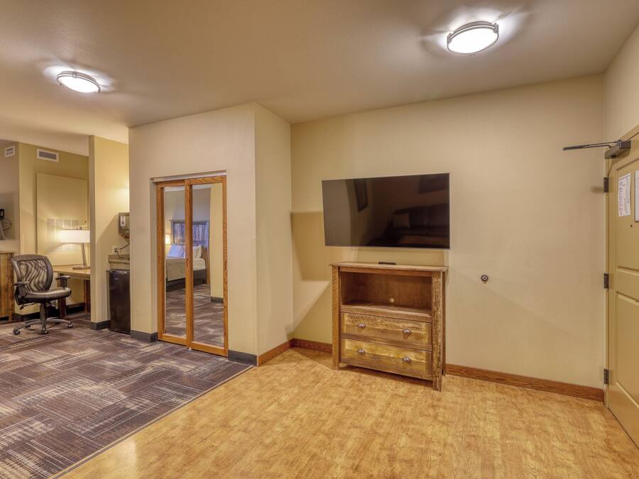 Ein Hotelzimmer mit Flachbildfernseher, einer Holzkommode, einem Schreibtisch mit Computer und Teppichboden.