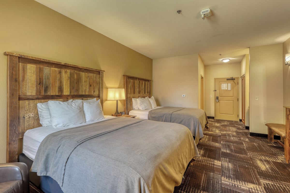 Habitación de hotel con dos camas, cabeceros de madera, piso cubierto de alfombra y una puerta que da a otra habitación.