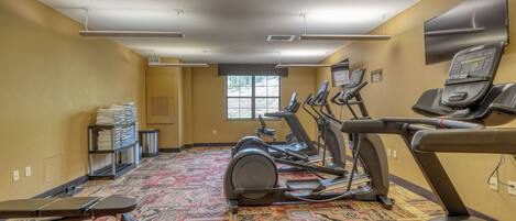 A gym with multiple treadmills, a stationary bike, and a wall-mounted television.