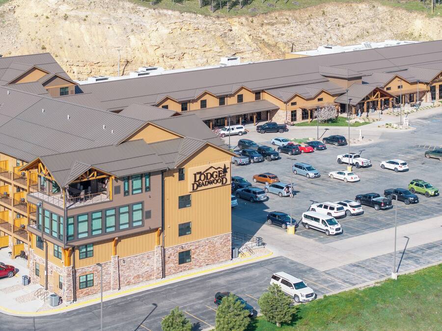 Un albergue con varias construcciones, un estacionamiento y montañas al fondo.