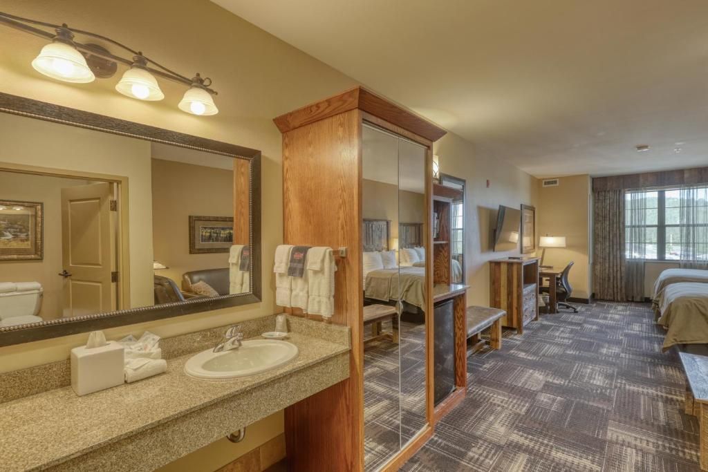 A hotel room with a large mirror, a sink, a bed, a desk, and a window.