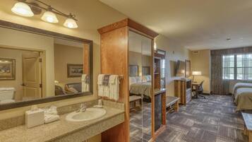A hotel room with a large mirror, a sink, a bed, a desk, and a window.