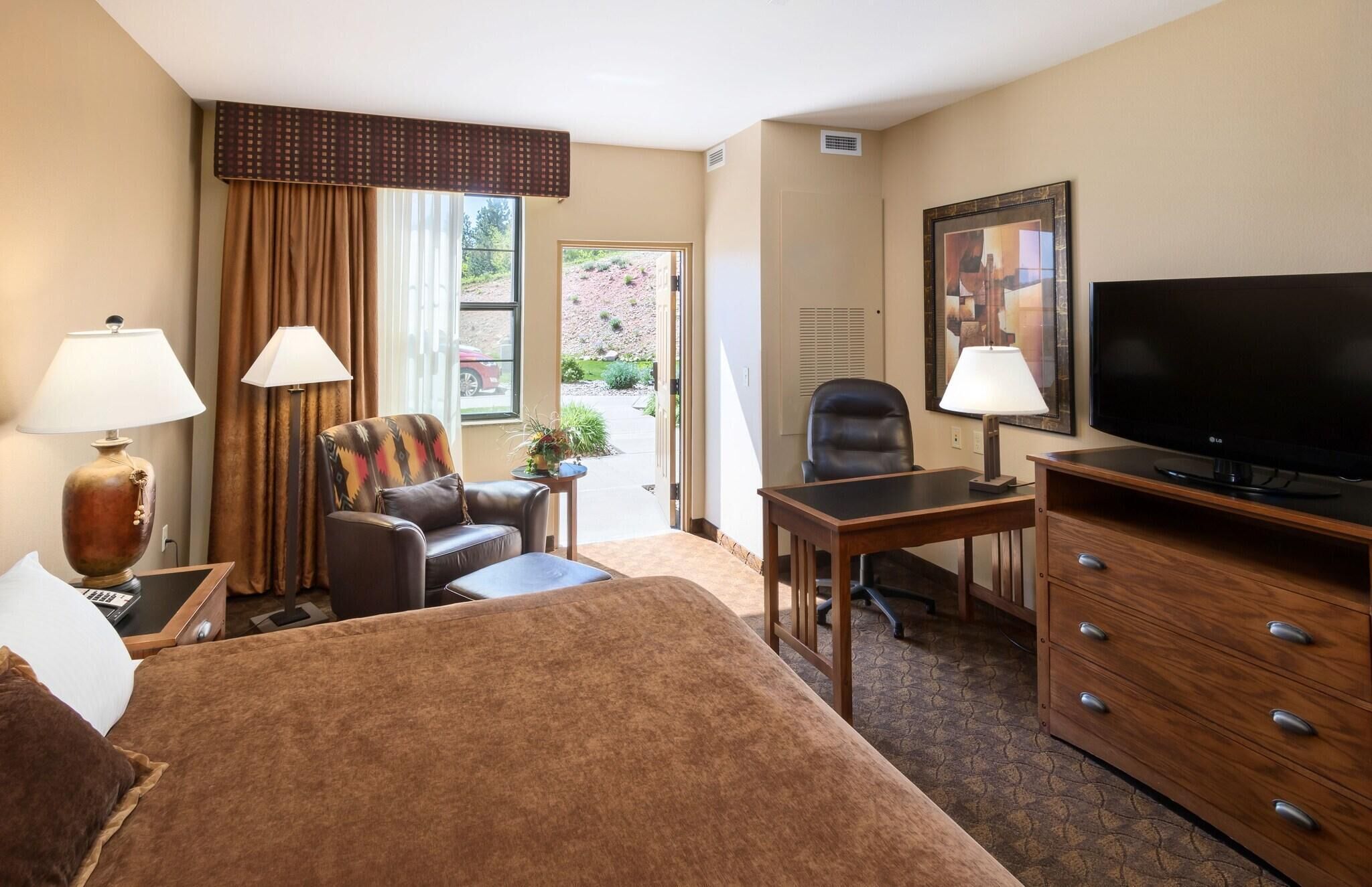 Ein Hotelzimmer mit Bett, Schreibtisch, Stuhl, Fernseher und einem Fenster mit Vorhängen.