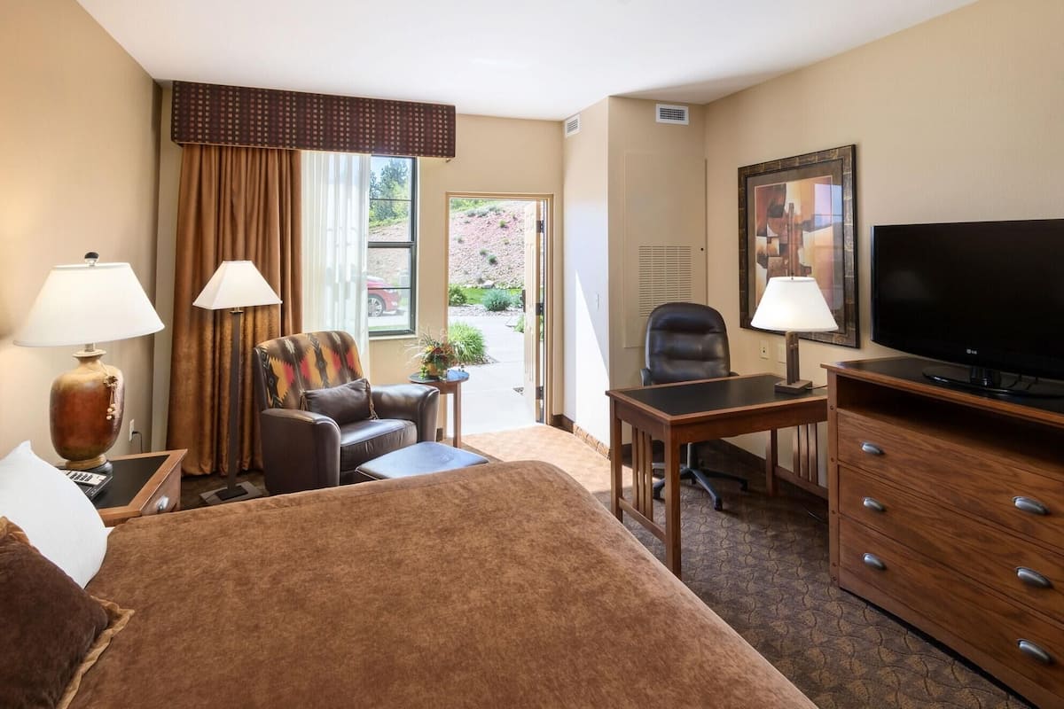 Habitación de hotel con cama, escritorio, silla, televisión y ventana con cortinas.