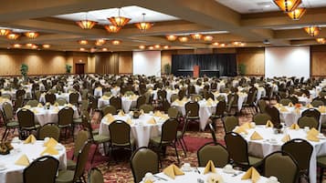 A large banquet hall with rows of tables set for a formal event, equipped with chandeliers and a stage.
