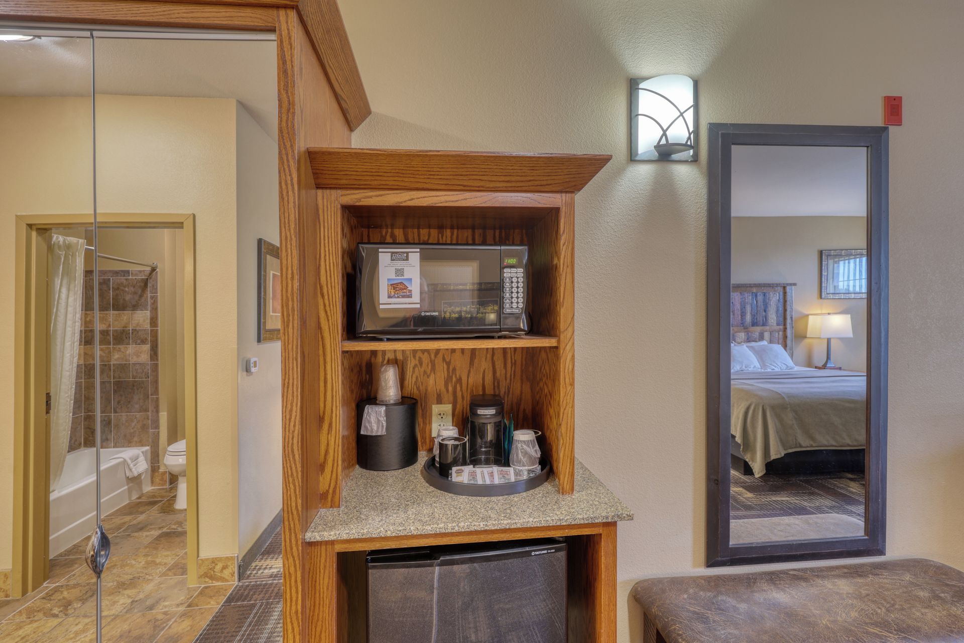 Habitación de hotel con repisa de madera que contiene un microondas, cafetera y otros servicios.
