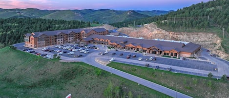A large hotel with multiple buildings, a parking lot, and a view of surrounding hills.