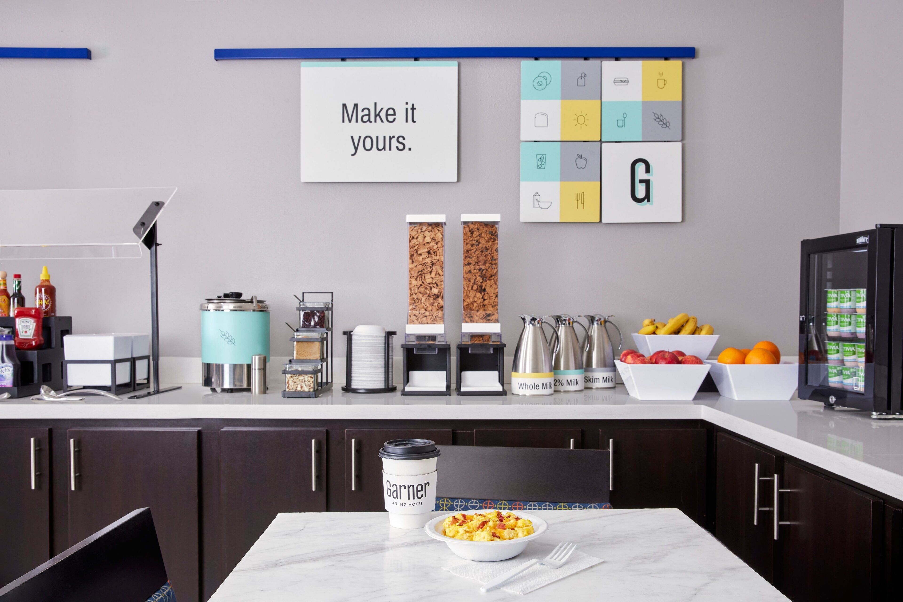 A modern kitchen with a marble countertop, a coffee machine, a kettle, and a bowl of cereal.