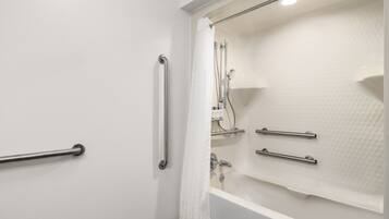A bathroom with a bathtub, a shower, and a handrail.