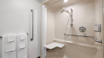 A bathroom with a shower, grab bars, a towel rack, and a soap dispenser.