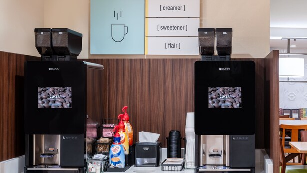 A coffee station with two Bunn coffee machines, a sign for adding cream, sweetener, or flairs, and various coffee-related items.