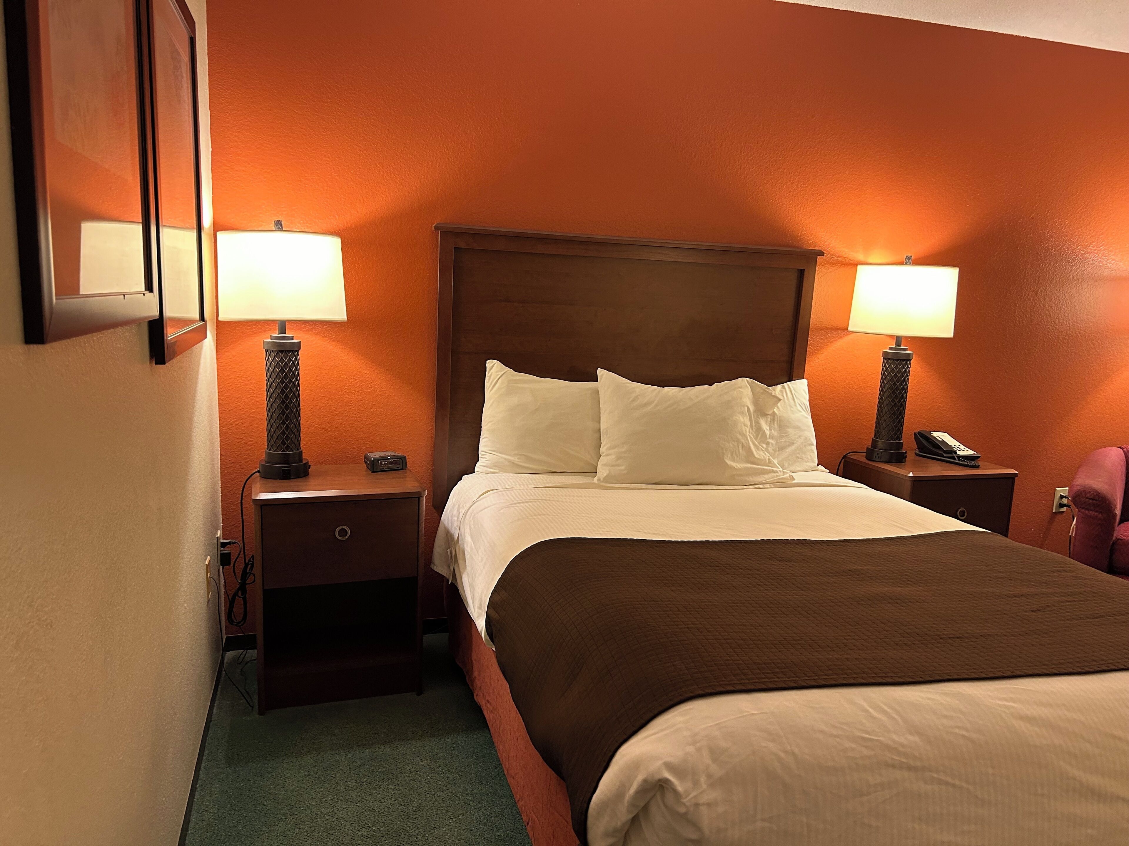 A hotel room with a large bed, two bedside tables with lamps, a telephone, and a wall-mounted TV.