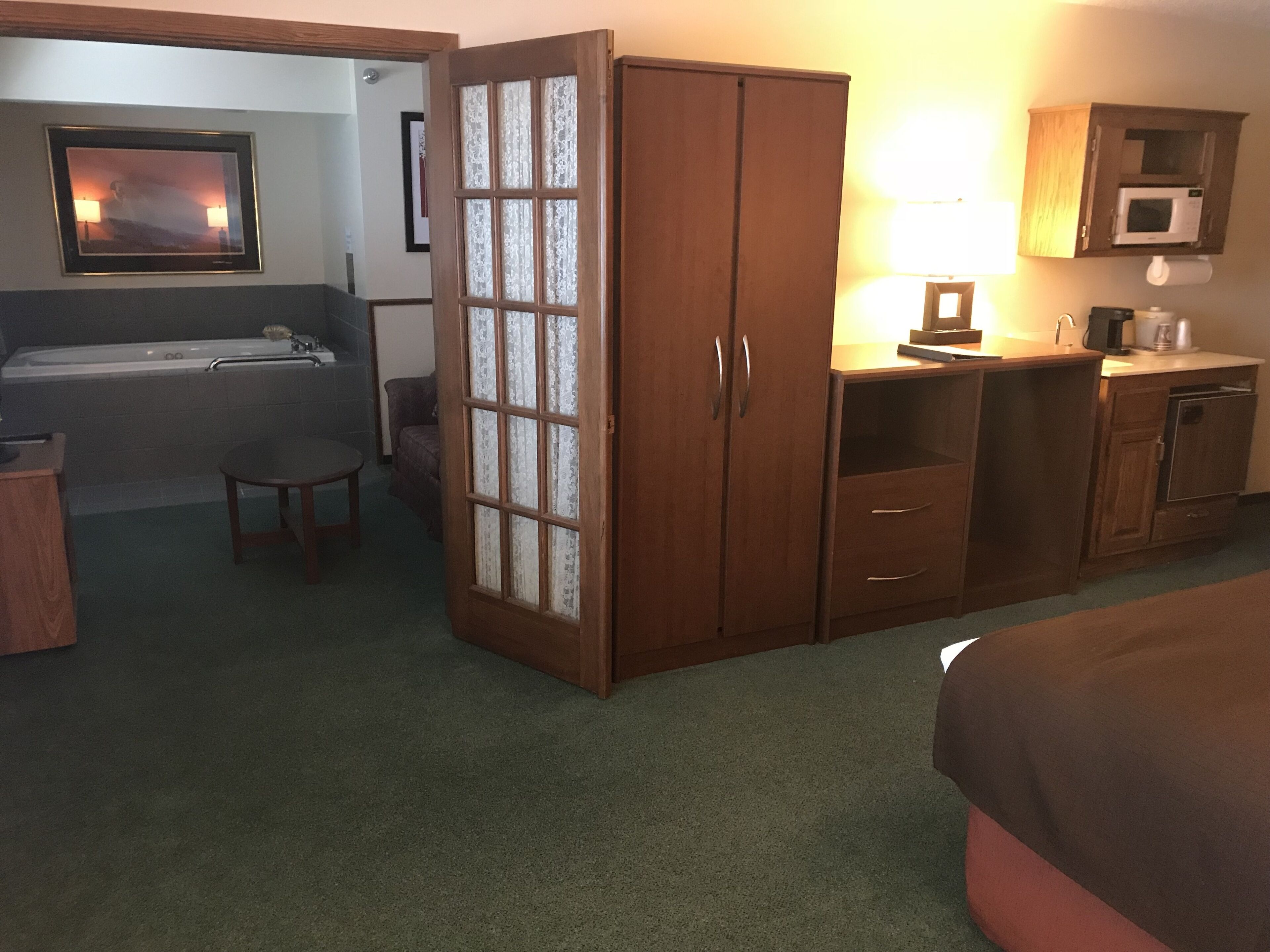 Ein Hotelzimmer mit Bett, Schreibtisch, Stuhl, kleinem Tisch, Schrank, Mikrowelle, Spüle und Badewanne.