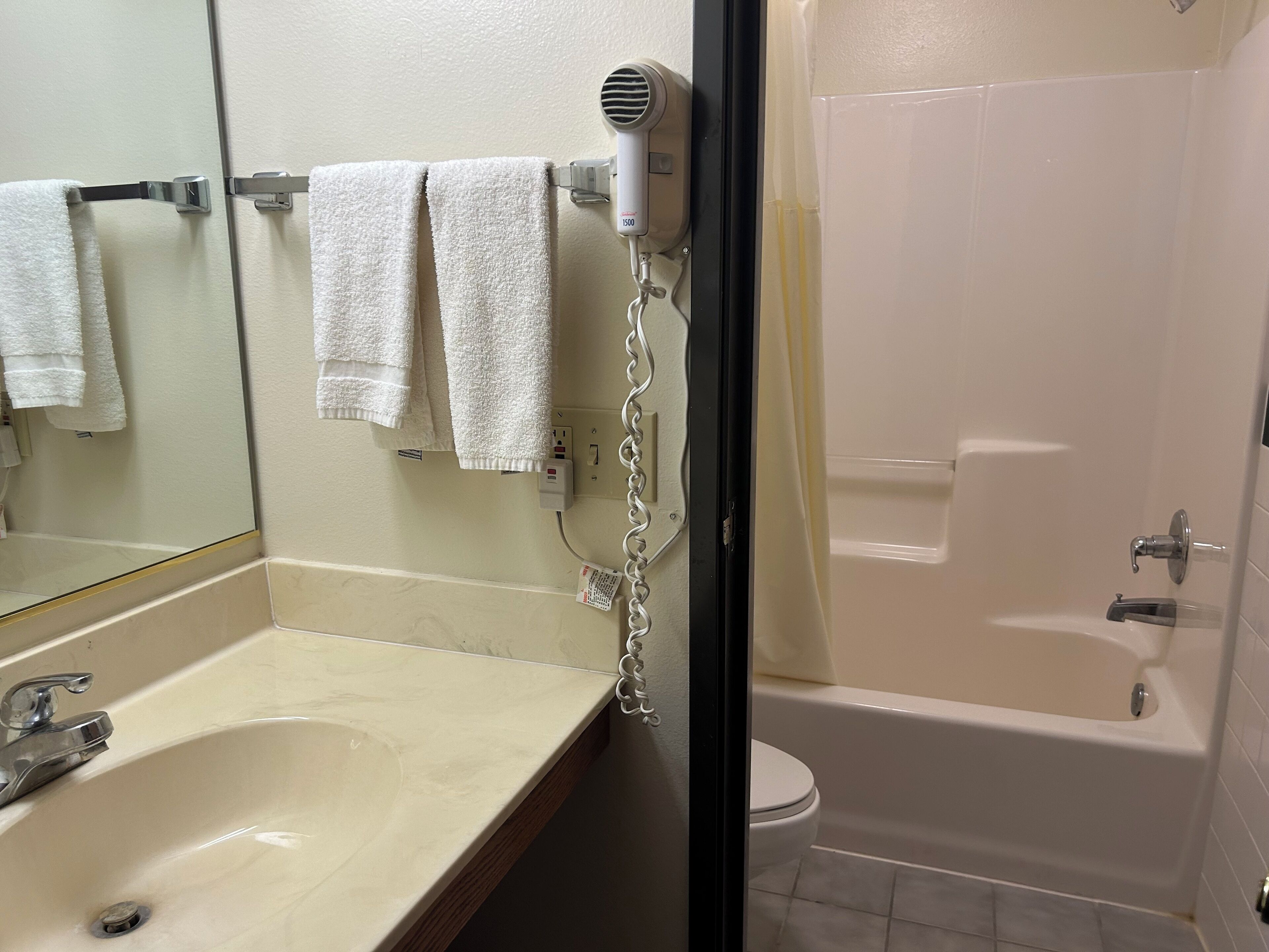 A bathroom with a sink, a mirror, a towel rack with towels, a hair dryer, and a bathtub.