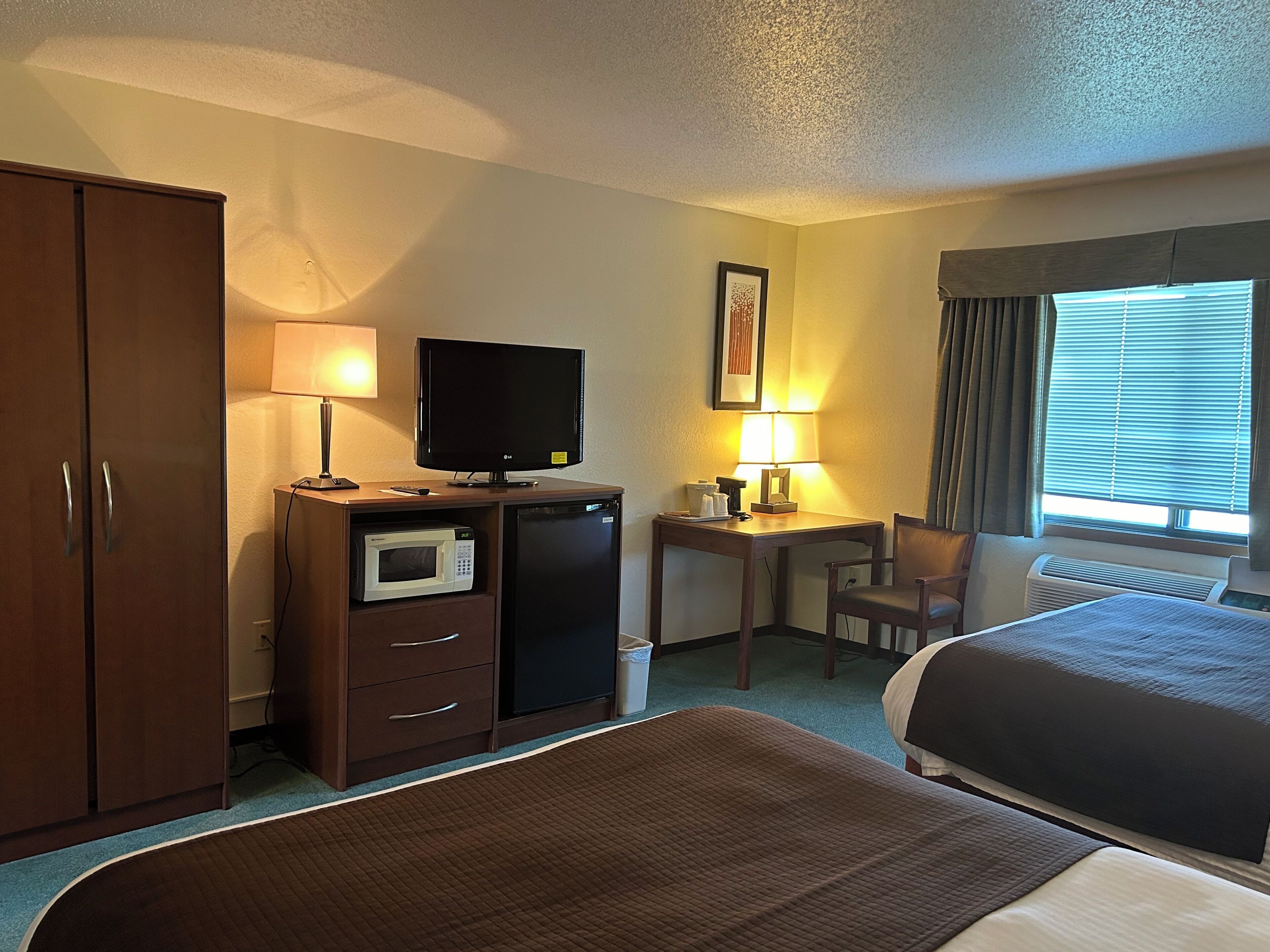 Een hotelkamer met een bed, een bureau met een computer, een televisie, een magnetron, een koelkast en een kledingkast.