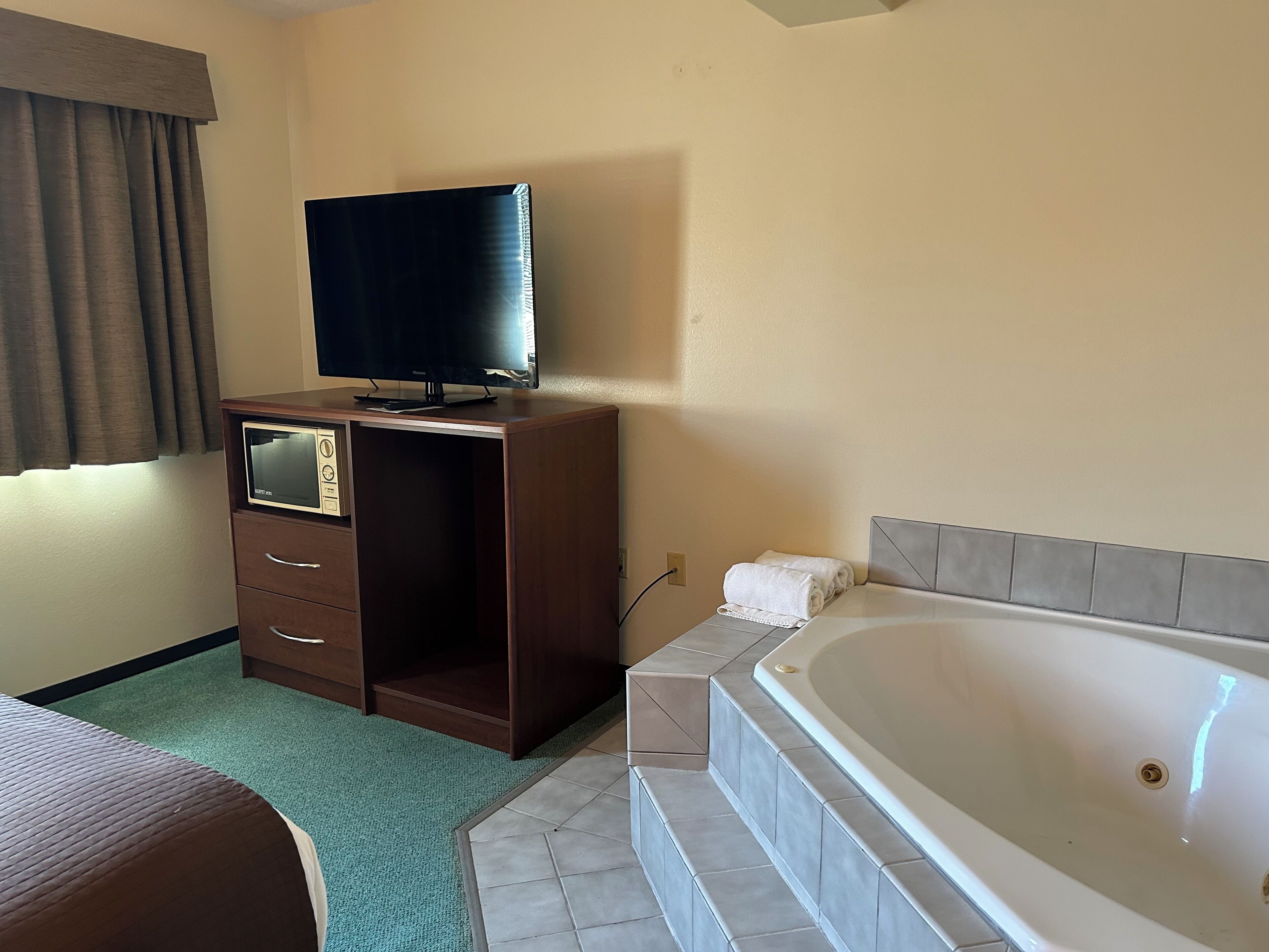Habitación de hotel con escritorio de madera, televisor de pantalla plana, bañera grande y alfombra verde.