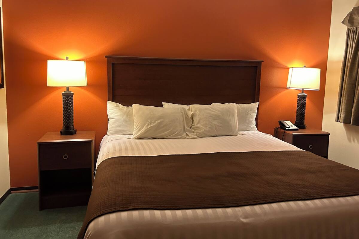 Quarto de hotel com uma cama grande, duas mesas de cabeceira e duas luminárias.