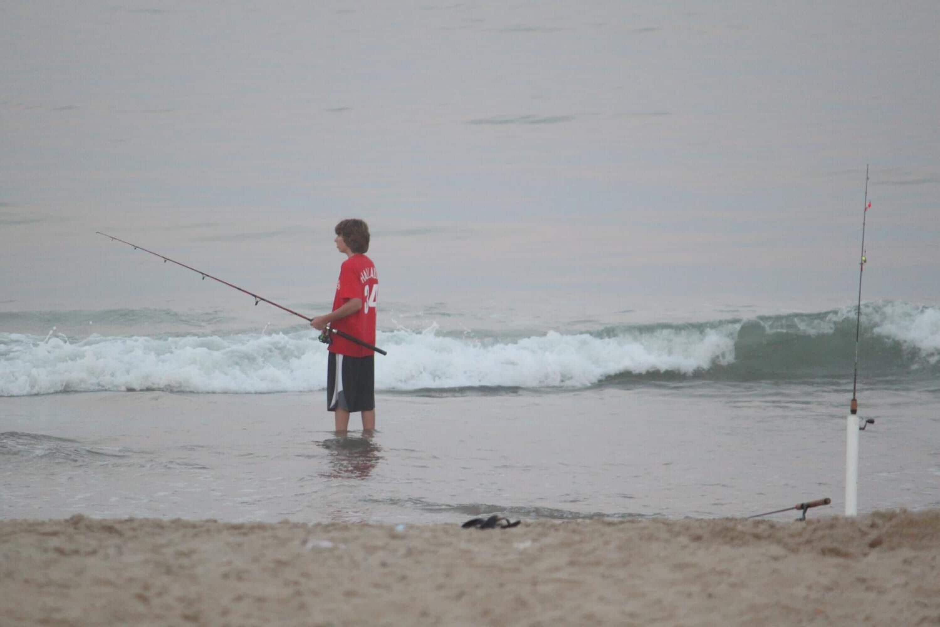 Iemand staat op het strand en houdt een hengel vast.