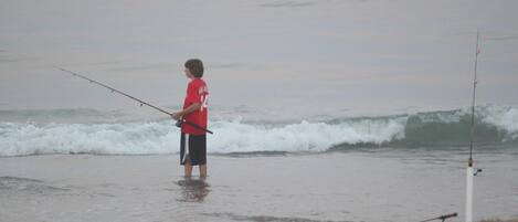 Iemand staat op het strand en houdt een hengel vast.