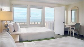 Habitación de hotel con dos camas, un escritorio, una silla y un amplio ventanal con vistas al mar.