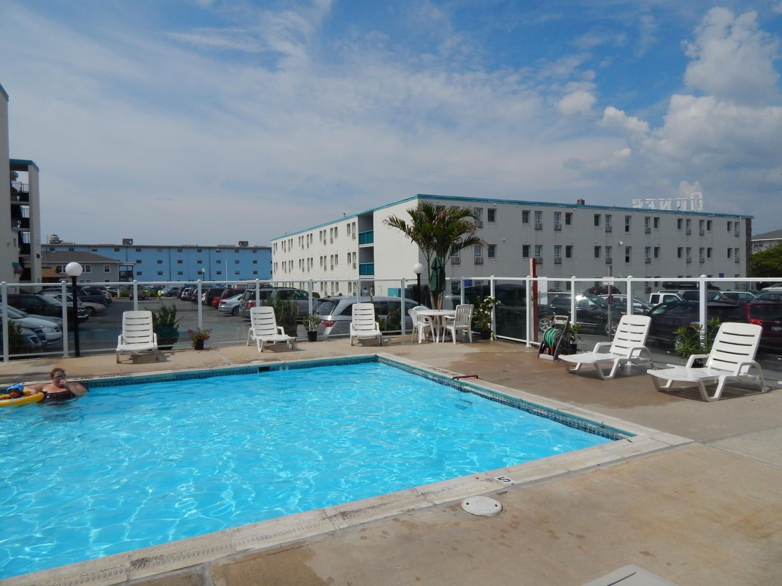 Una piscina con sillas de descanso y vista a un estacionamiento y edificios al fondo.