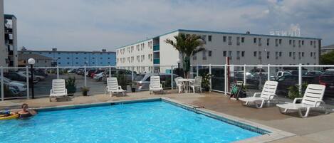 A swimming pool with lounge chairs and a view of a parking lot and buildings in the background.