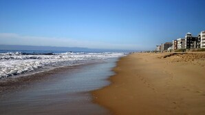 Una playa con arena y olas. Hay edificios a lo largo de la playa.