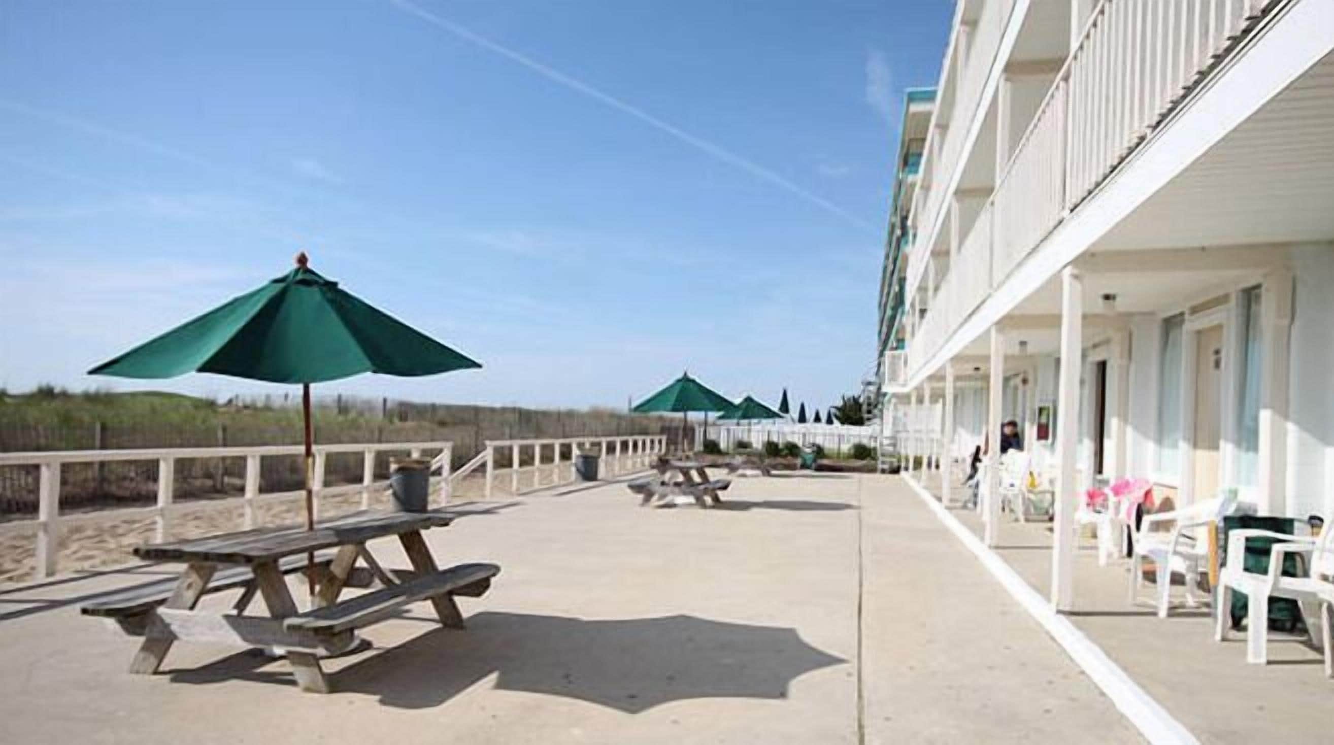 A beachfront hotel with outdoor seating and umbrellas, a boardwalk, and a beach in the background.