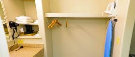 A small bathroom with a countertop, a mirror, a shelf with towels, a hanging rack, and a towel rack.