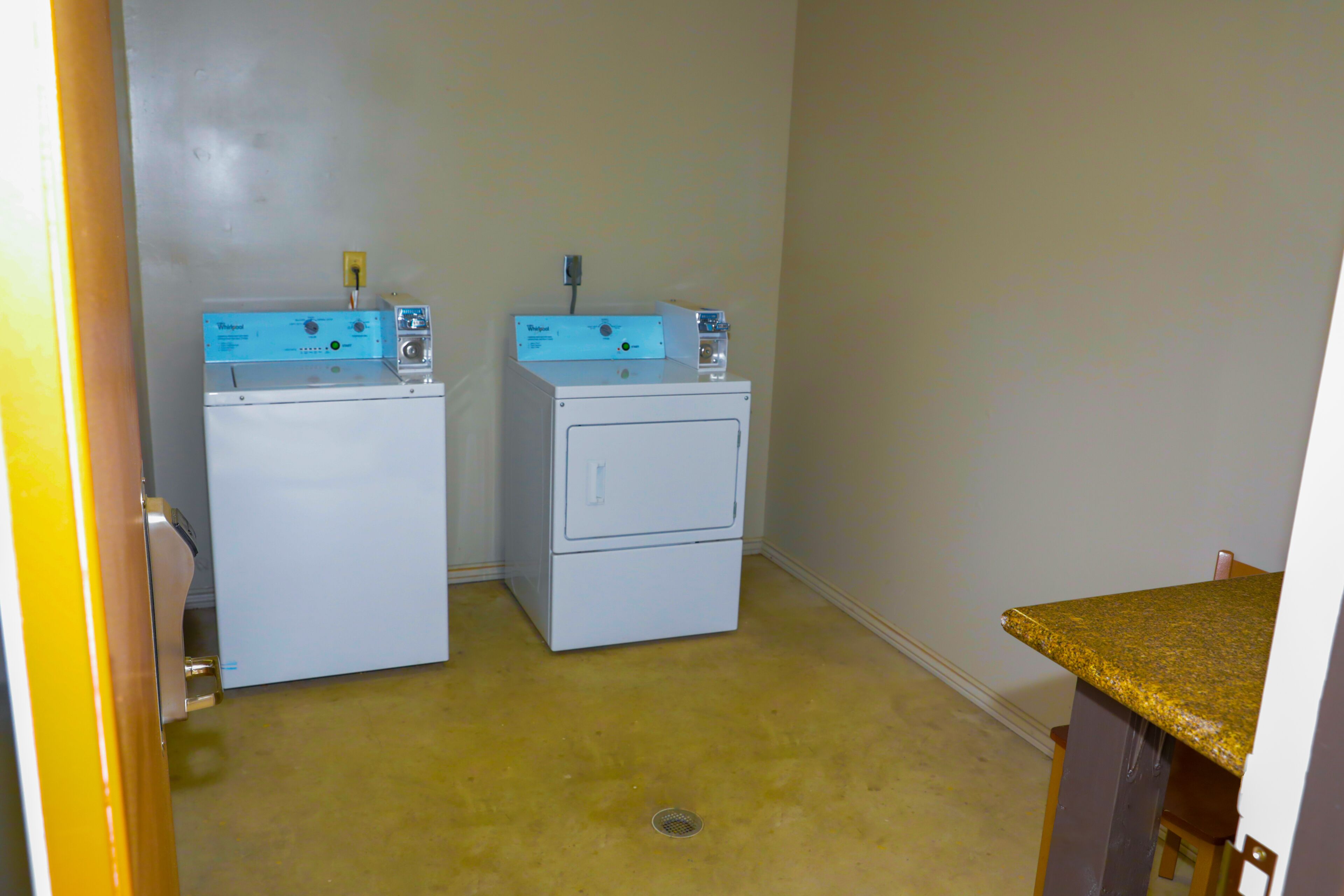 A laundry room with two stacked washers and dryers, a wooden chair, and a yellow countertop.