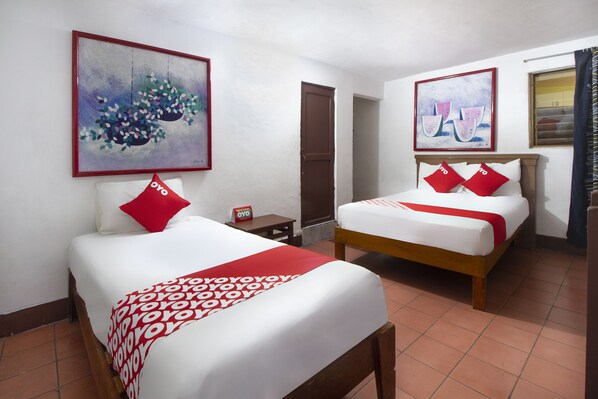 A hotel room with two beds, each with red and white bedding, a small table, and a framed artwork on the wall.