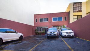 A parking area with three cars parked in front of a building with a red and white facade. - OYO Hotel Brazil,Guadalajara,Estadio Jalisco (Guadalajara)