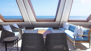 A sunlit outdoor seating area with a view of the sea, featuring wicker furniture and a wooden table. - Double-Six Luxury Hotel (Seminyak)