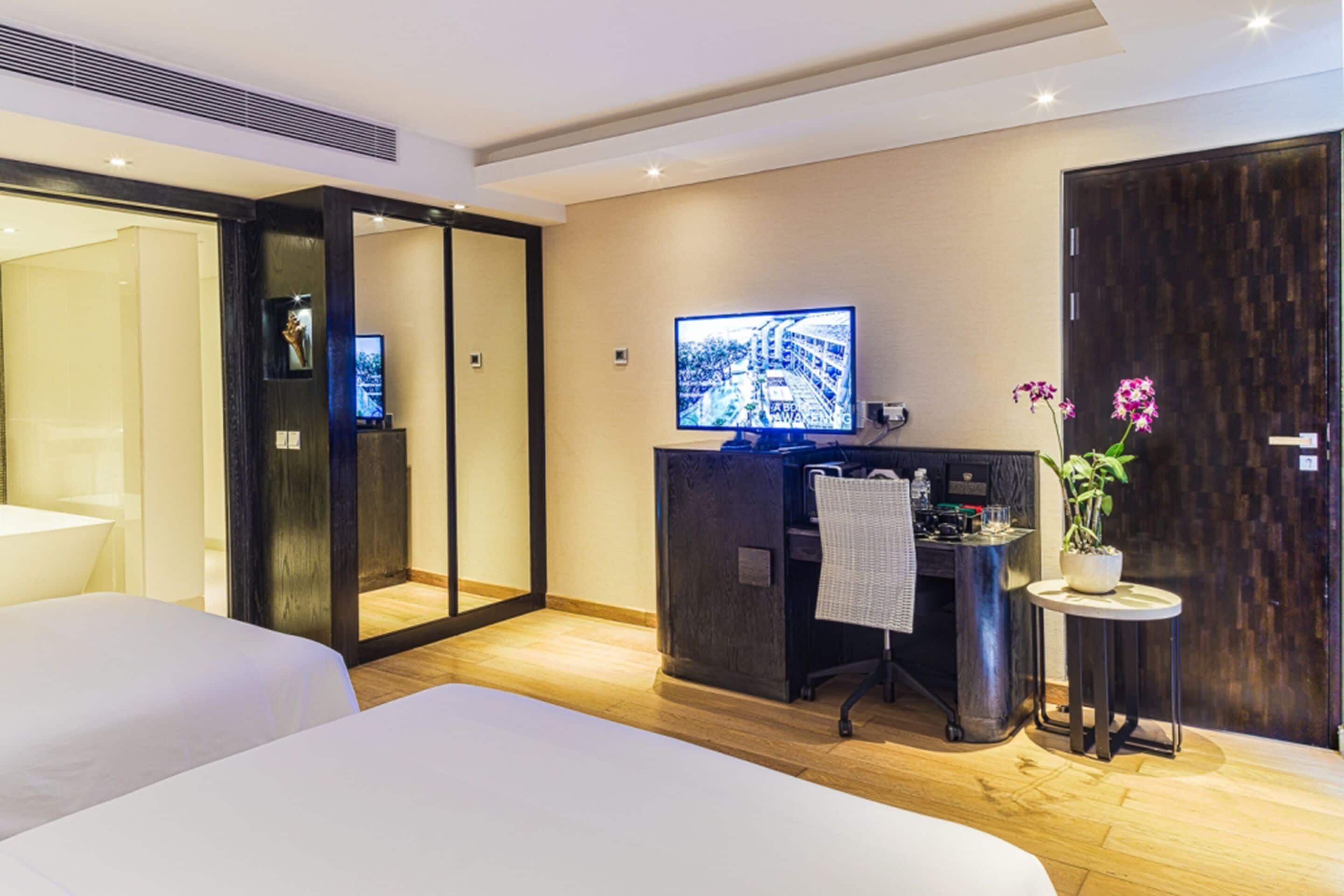 Une chambre d’hôtel avec un lit, un bureau avec un ordinateur, une télévision et une petite table avec une plante.