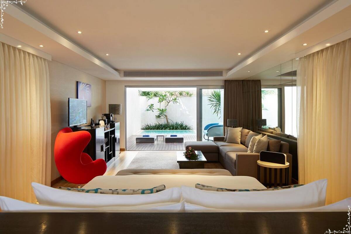A modern hotel room with a large bed, a red armchair, a sofa, a small table, and a TV.