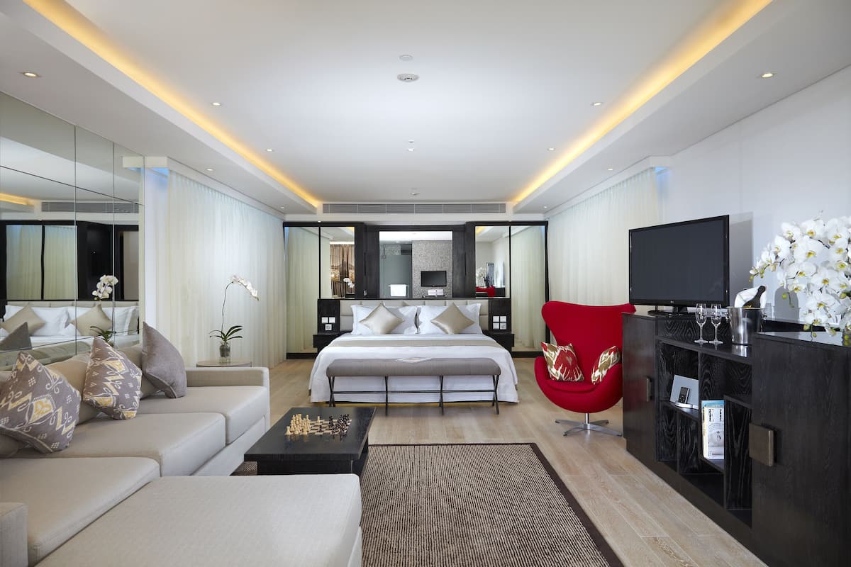 A modern hotel room with a large bed, a red armchair, a television, and a minibar.