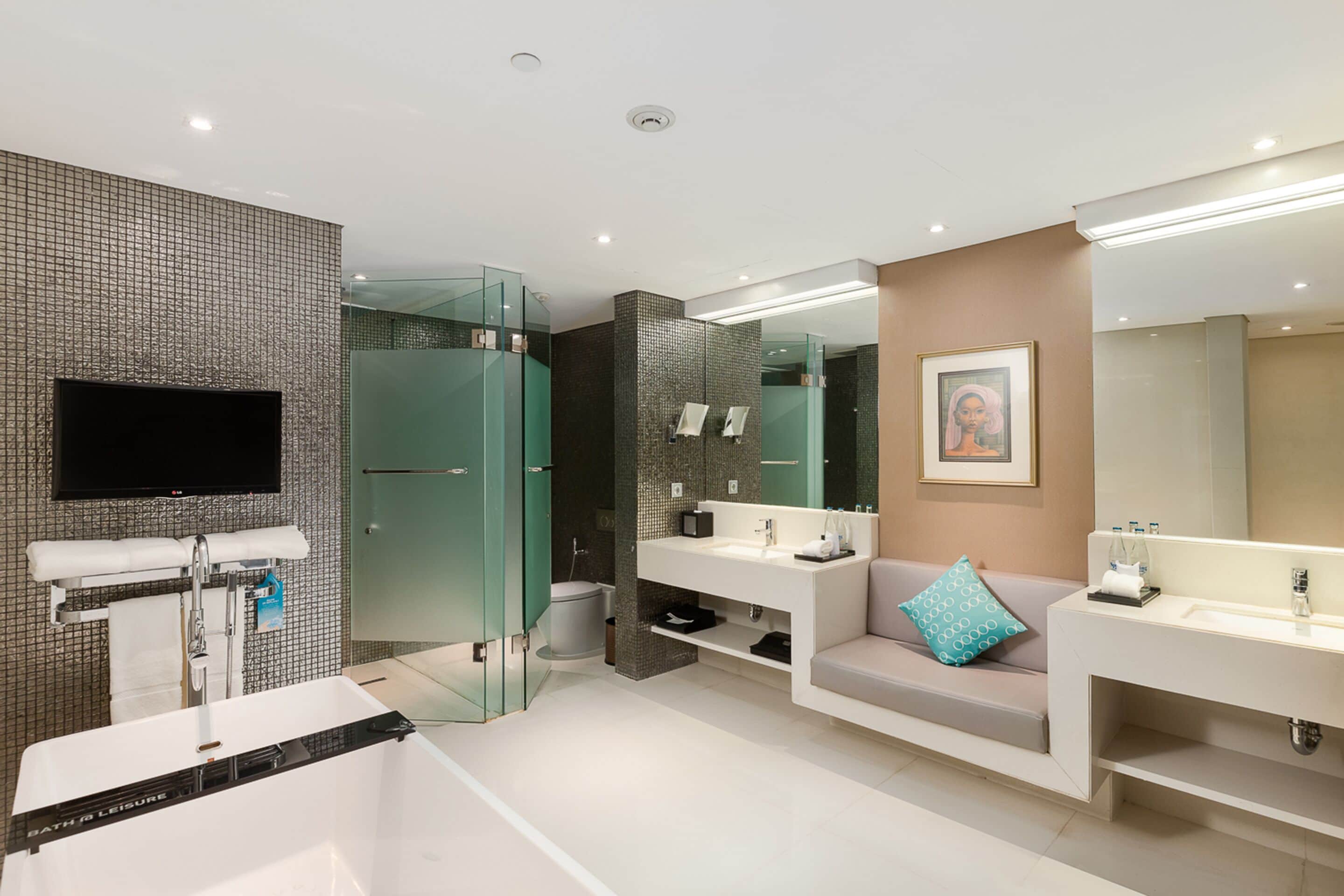 Une salle de bain moderne dotée d’une douche à parois de verre, d’un grand miroir et d’un téléviseur à écran plat fixé au mur.