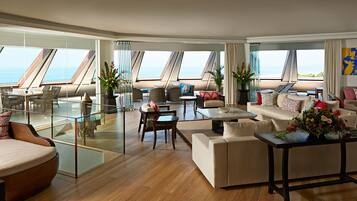 A spacious living area with a large glass wall, a sofa set, a coffee table, and a dining area with a view of the sea.