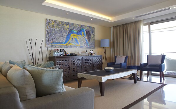 A modern living room with a sofa, a coffee table, a cabinet with bottles, and a painting on the wall.