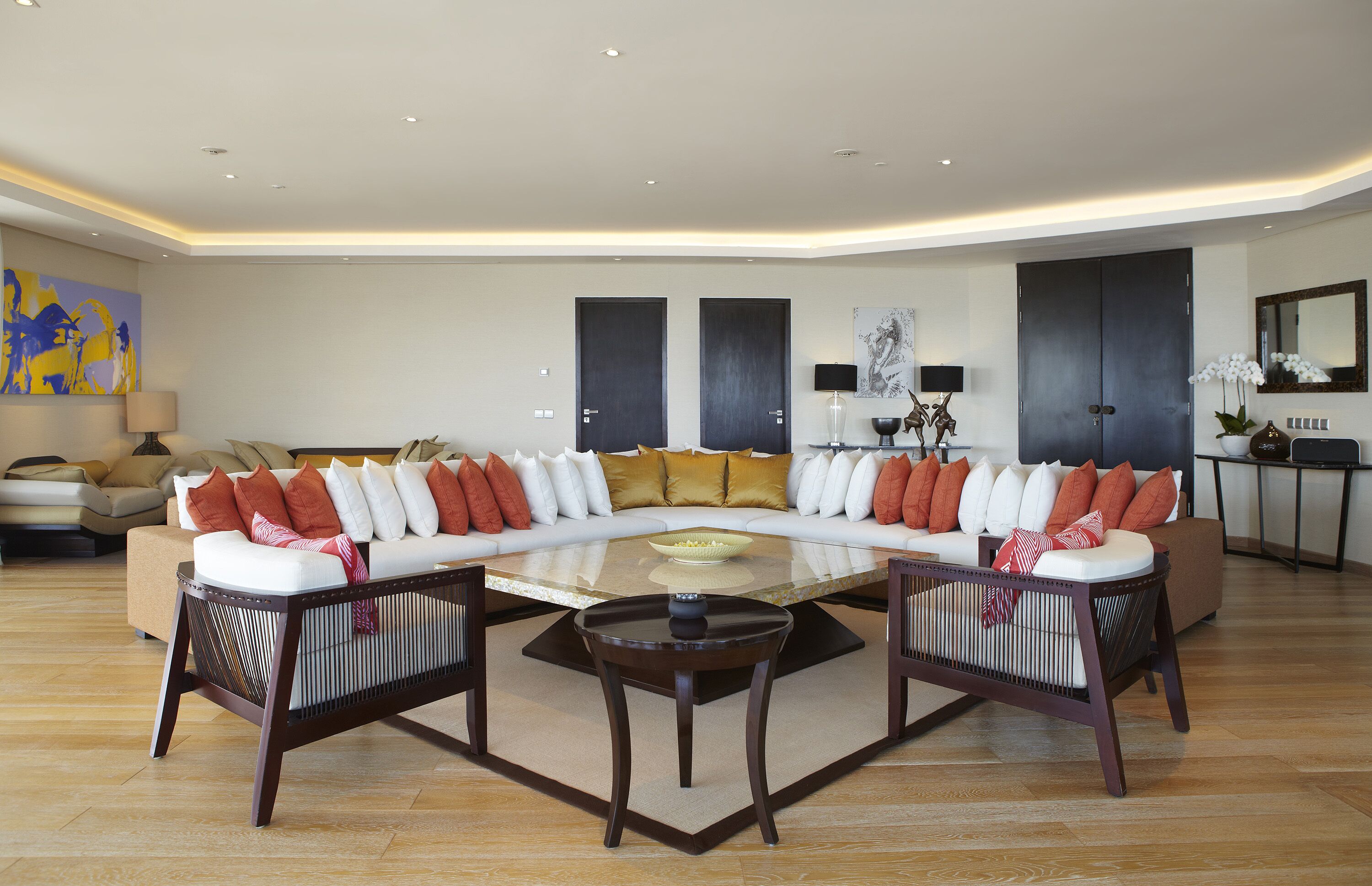 A modern living room with a large L-shaped sectional sofa, a glass coffee table, and a dining table with chairs.