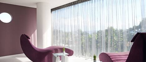 A modern room with two purple chairs, a glass table, and a large window with sheer curtains.