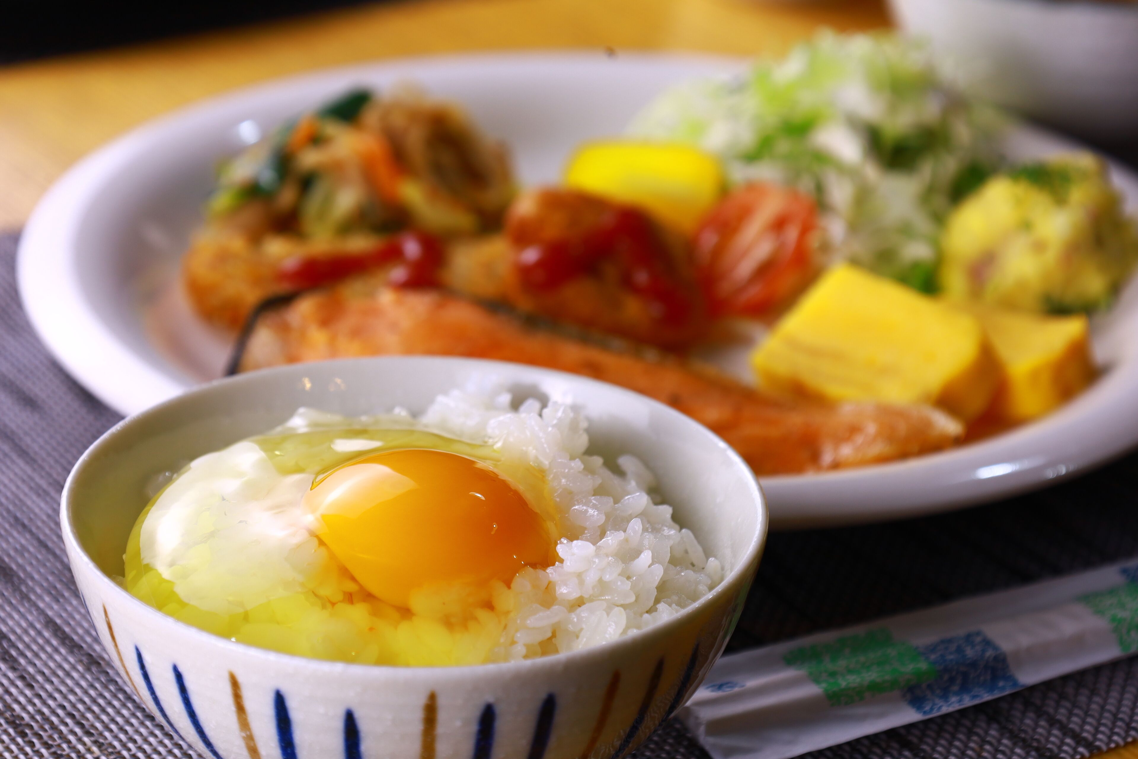 Un bol de riz garni d’un œuf, une assiette contenant divers aliments et une serviette.