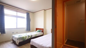 A room with two beds, a window with curtains, a door, and a wooden floor.