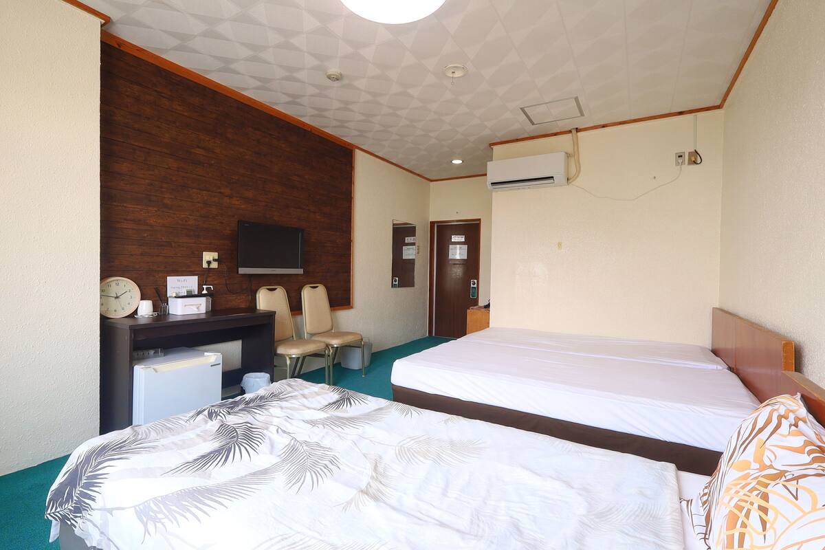 Ett hotellrum med två sängar, ett skrivbord med en tv, en klocka och en luftkonditioneringsanläggning.