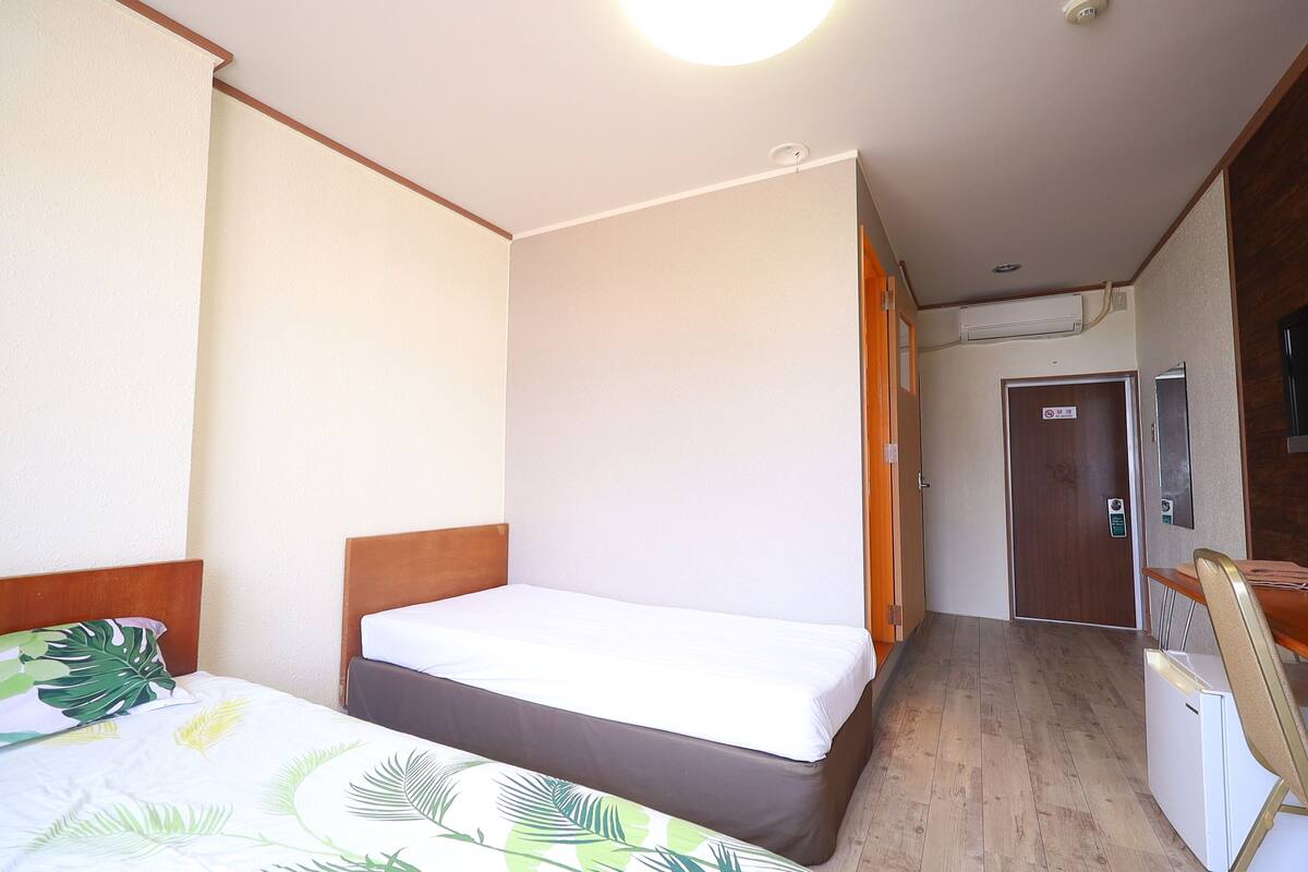 Ett hotellrum med en säng, ett skrivbord, en stol, en dörr och en luftkonditioneringsanläggning.
