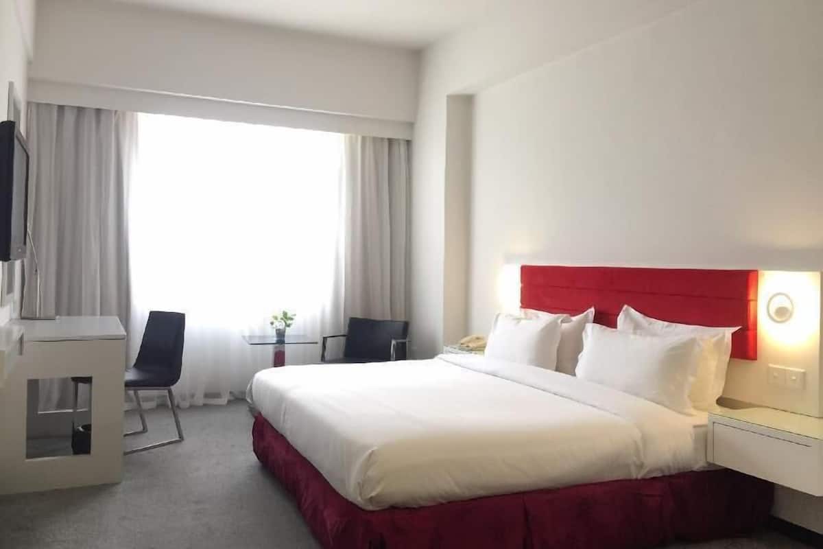 A hotel room with a bed, a desk, a chair, and a window with curtains.