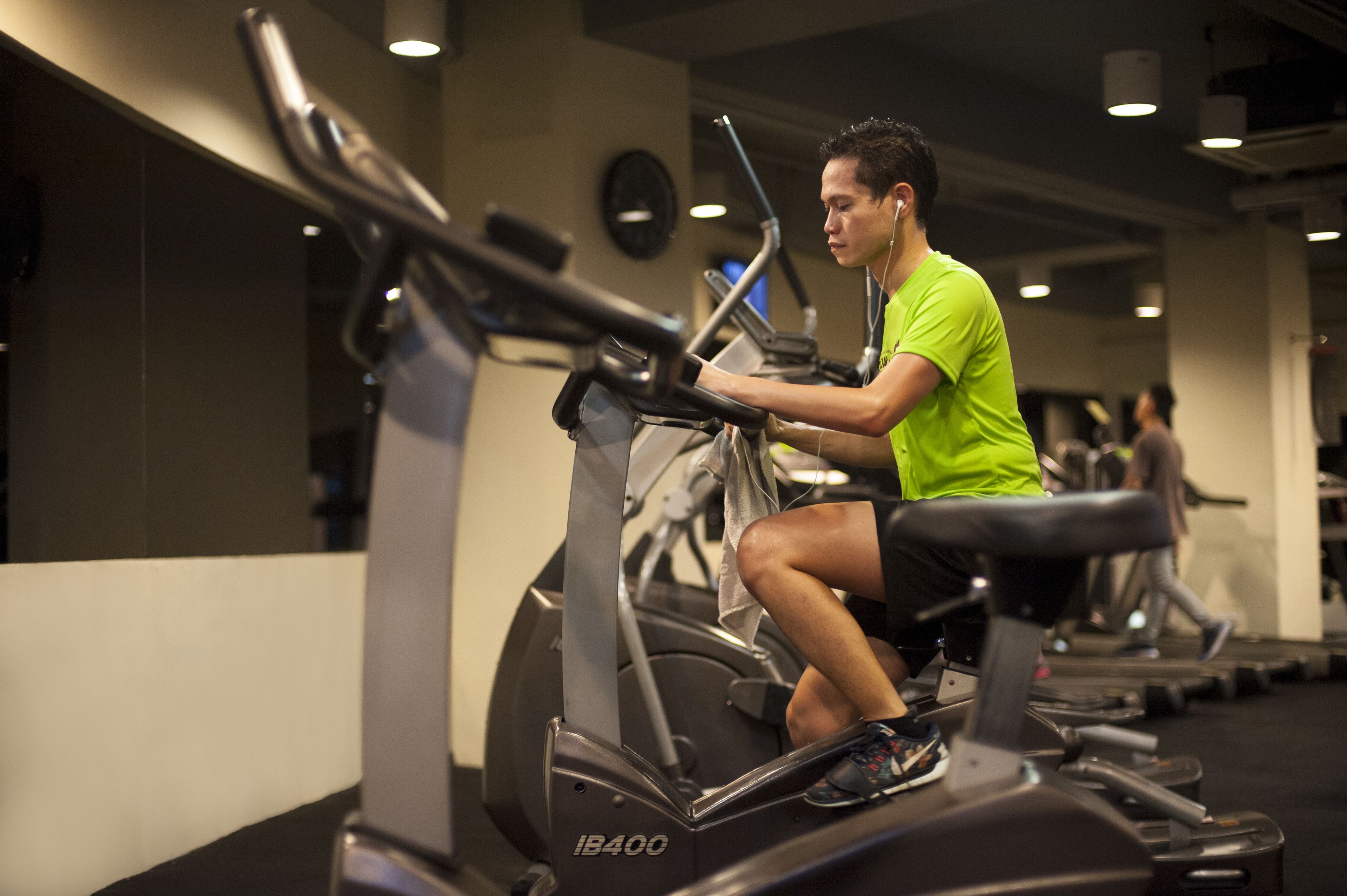 Un gimnasio con bicicletas estáticas, un reloj en la pared y una persona usando una máquina de ejercicio.