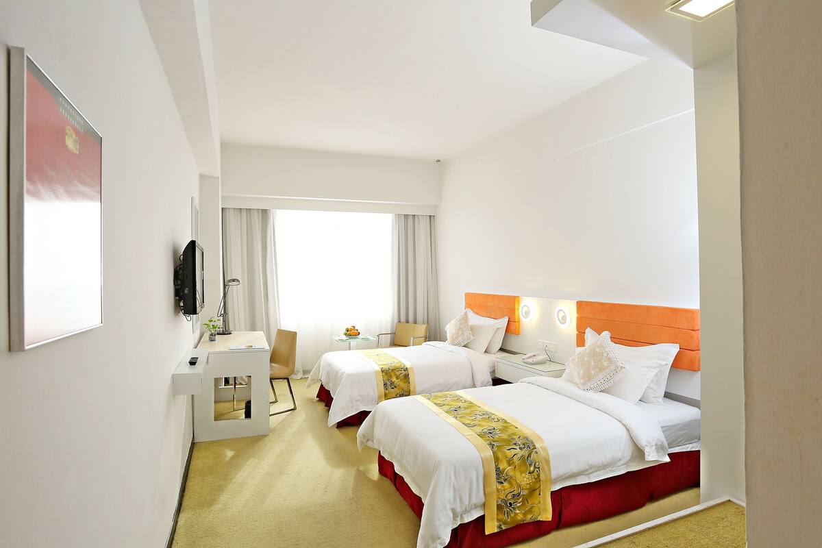 A hotel room with two beds, a desk, a chair, and a window with curtains.