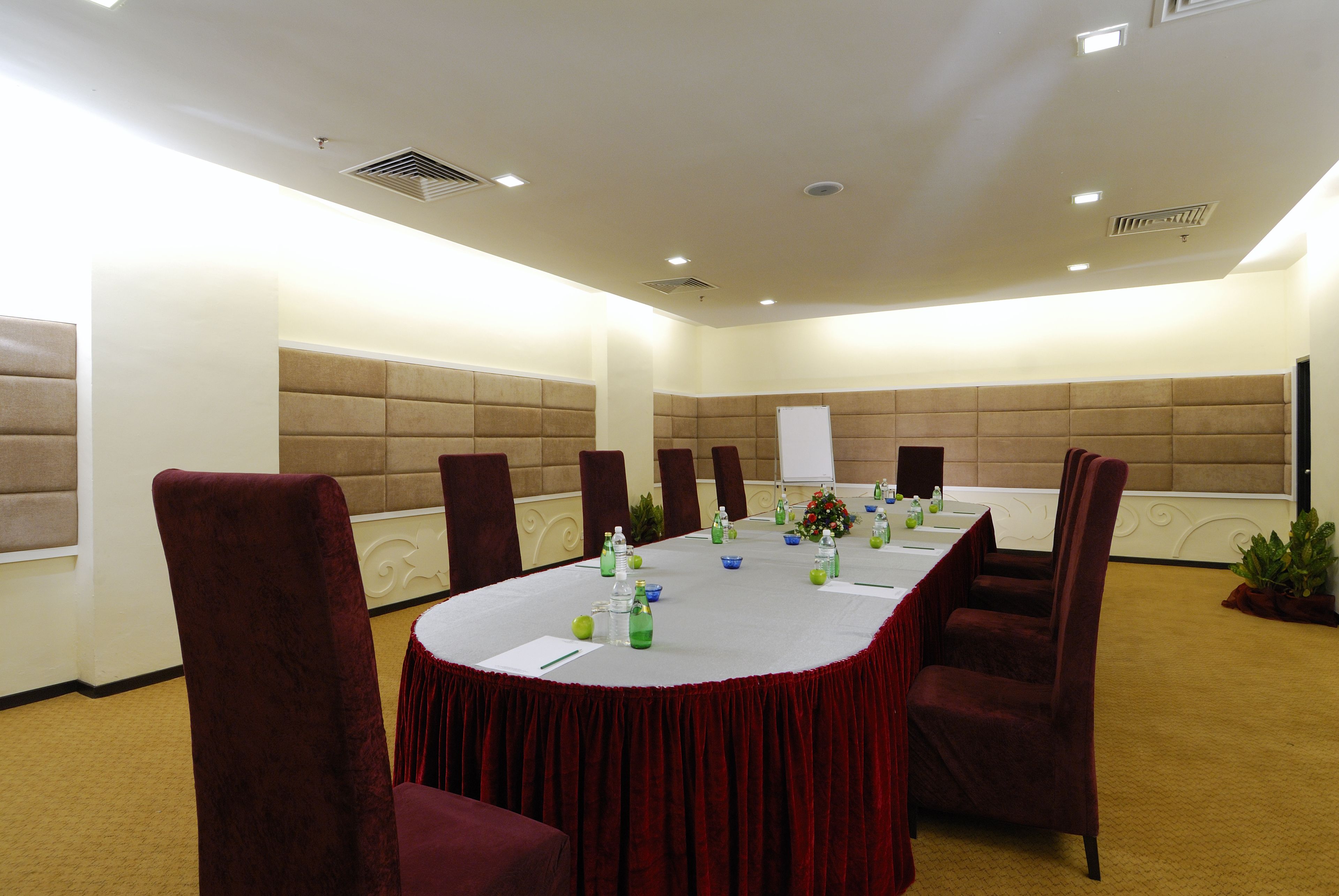 Une salle de conférence avec une longue table, des chaises rouges et un tableau blanc.